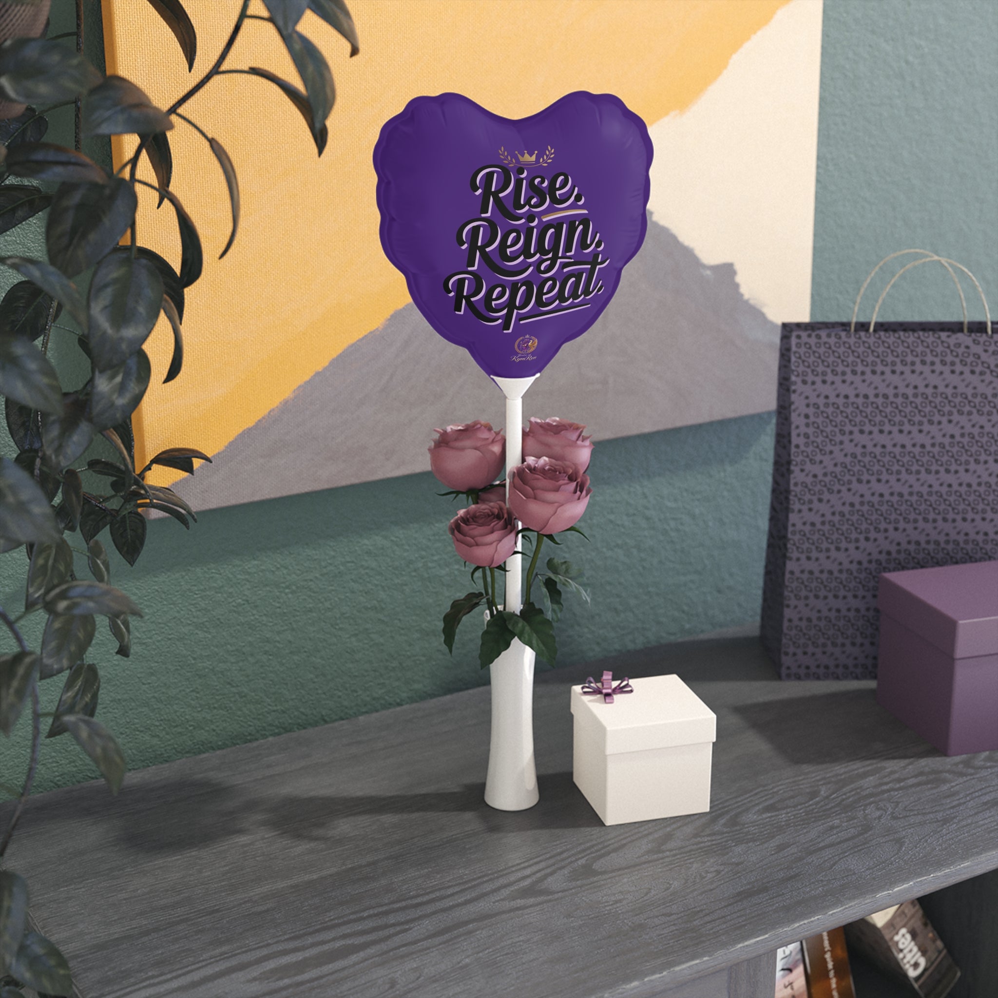 Purple balloon with 'Rise, Reign, Repeat' text, roses, and a white box on a table against a colorful wall.