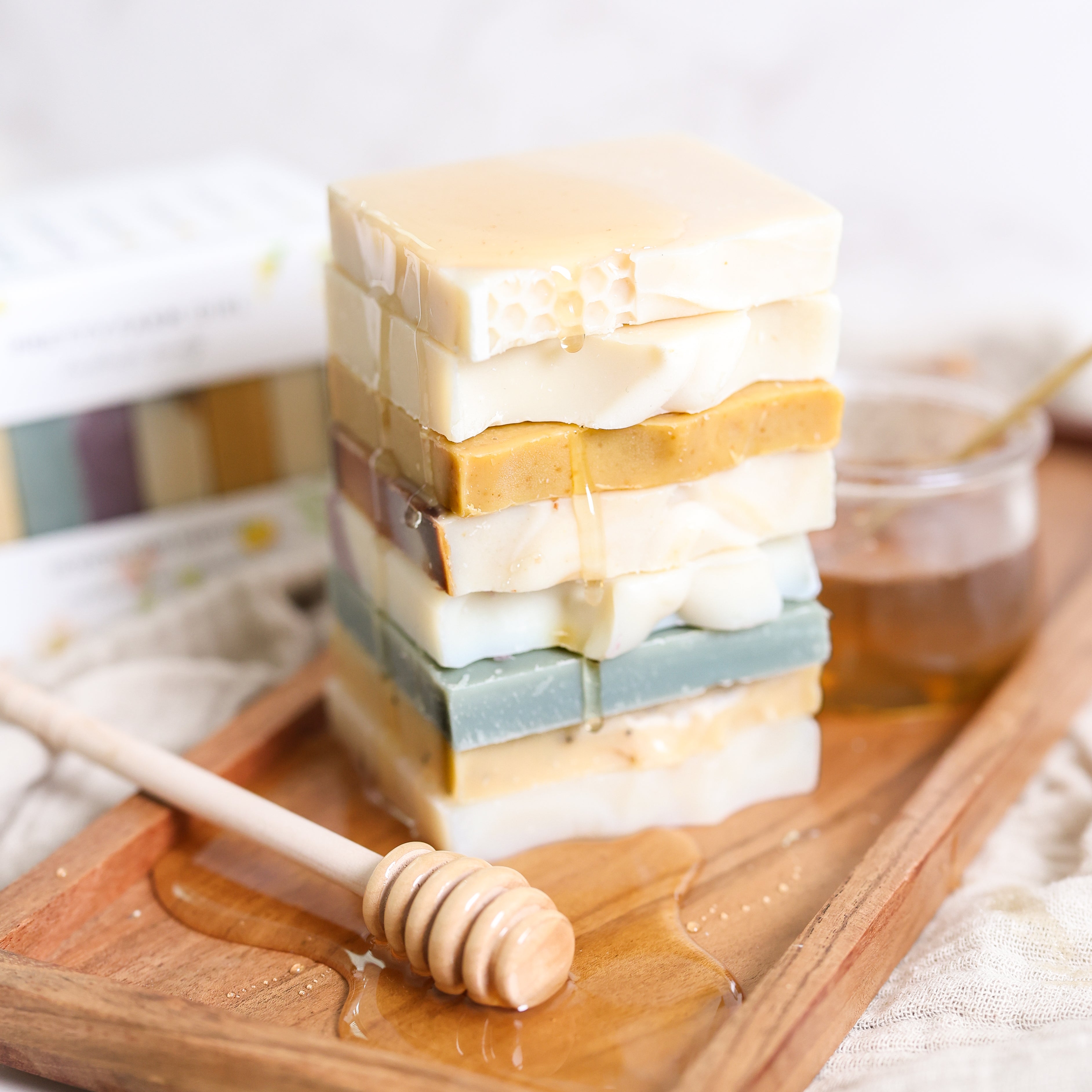 Stack of layered soap bars with a honey dipper on a wooden tray