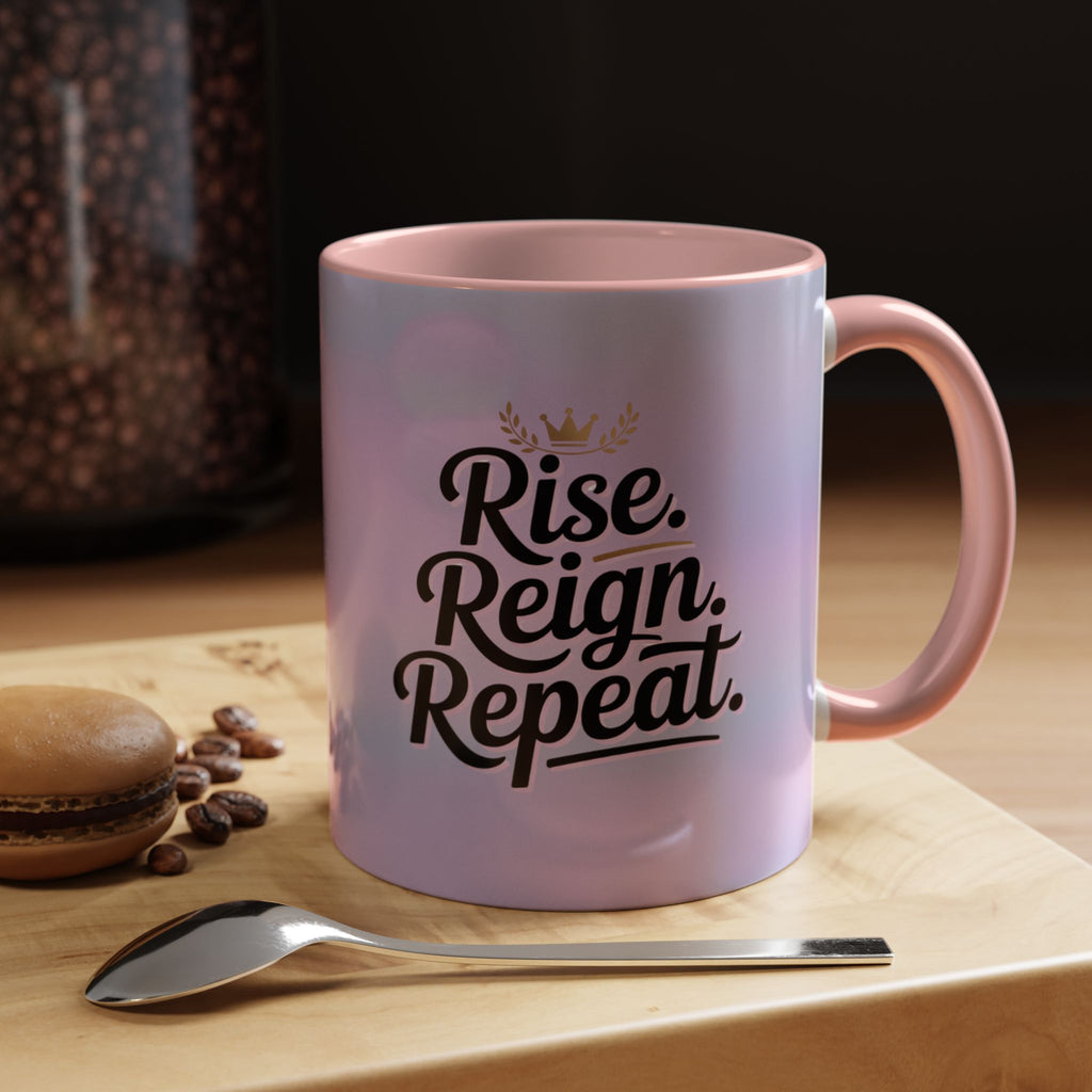 Pink mug with 'Rise. Reign. Repeat.' text on a wooden surface with coffee beans and a spoon.