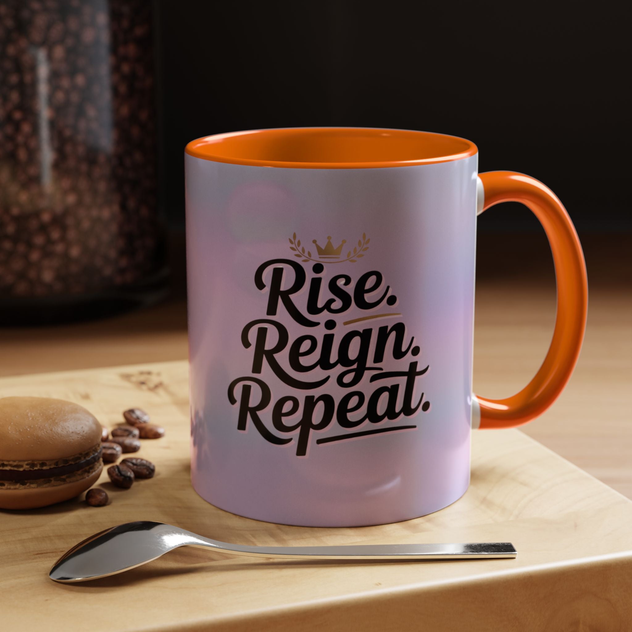Mug with 'Rise. Reign. Repeat.' text on a wooden surface with coffee beans and a spoon.