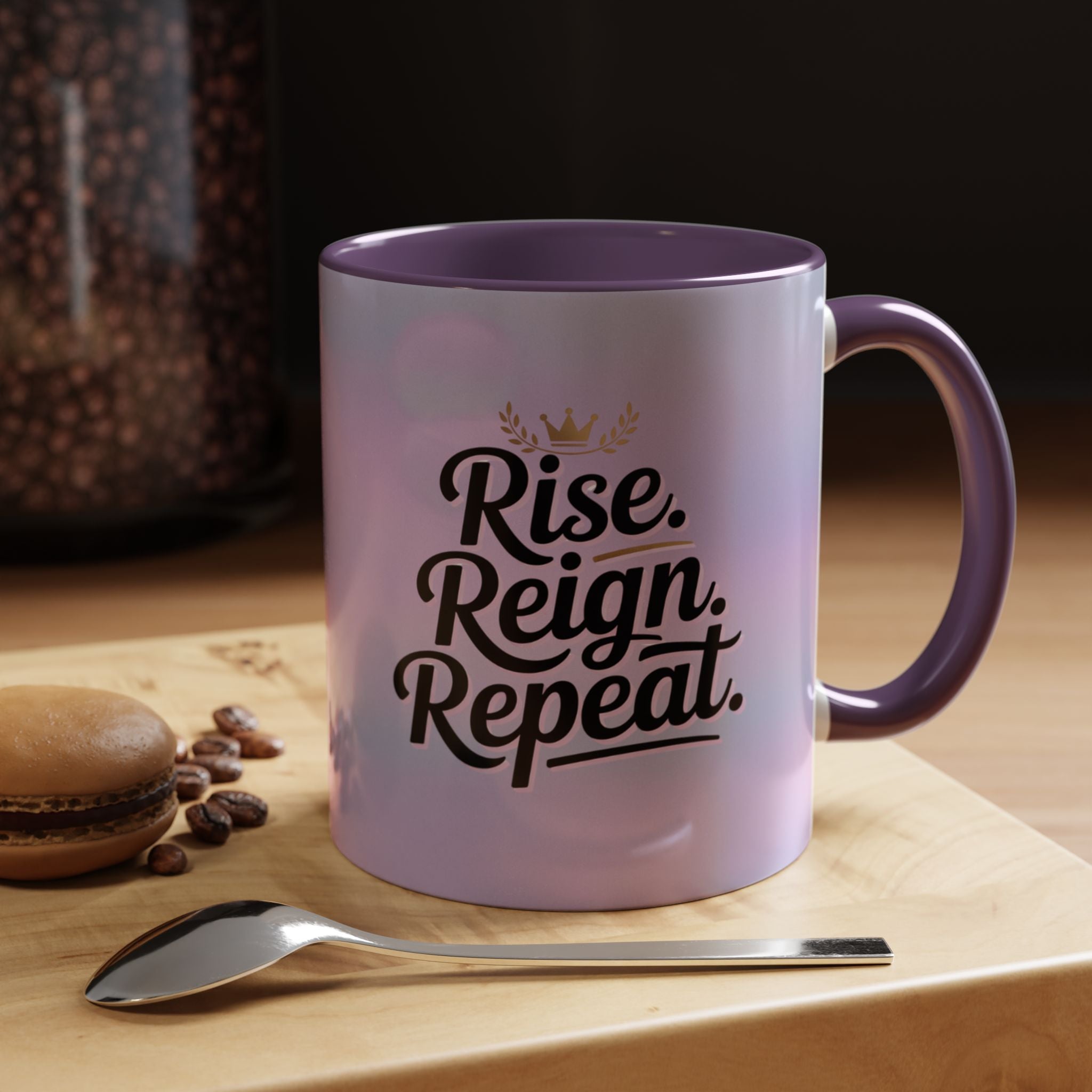 Purple mug with 'Rise. Reign. Repeat.' text on a wooden surface with coffee beans and a spoon.