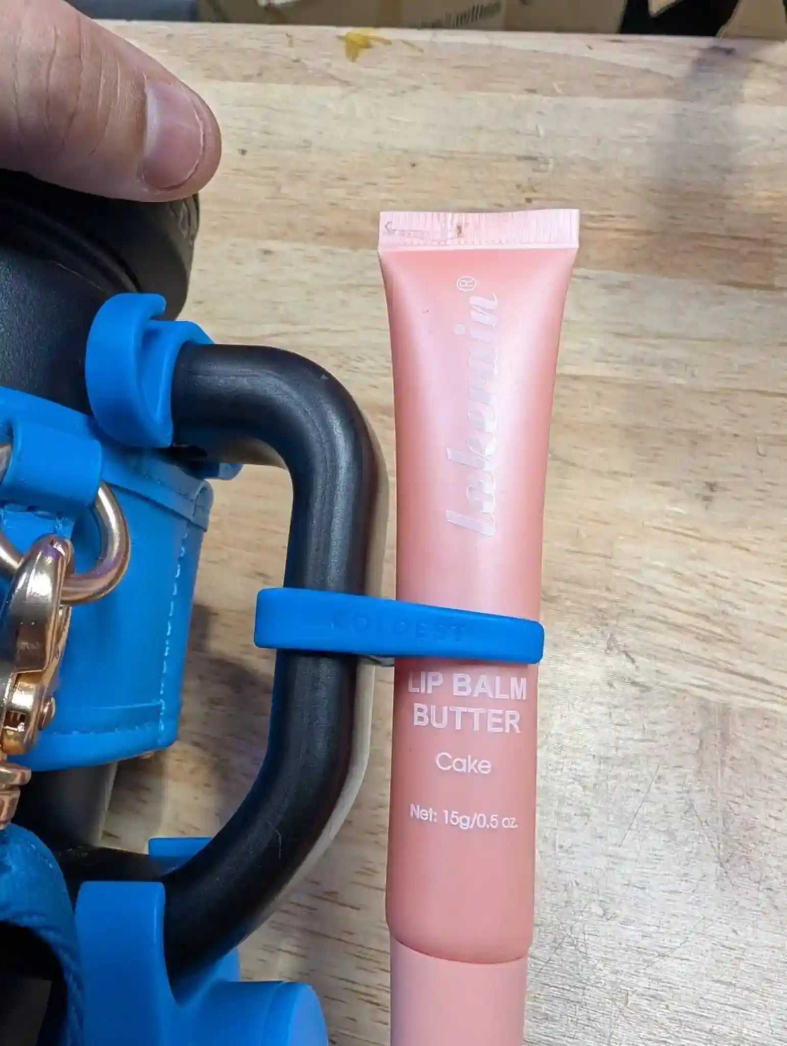 Pink lip balm tube with blue applicator on a wooden surface