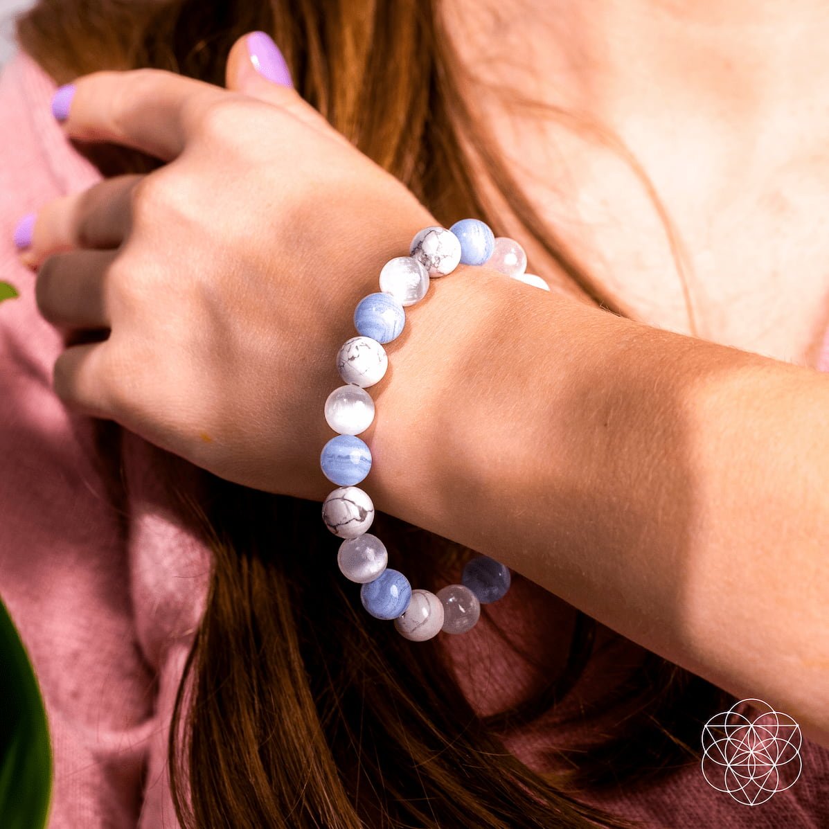 Close-up of a person wearing a blue and white beaded bracelet on a pink fabric background
