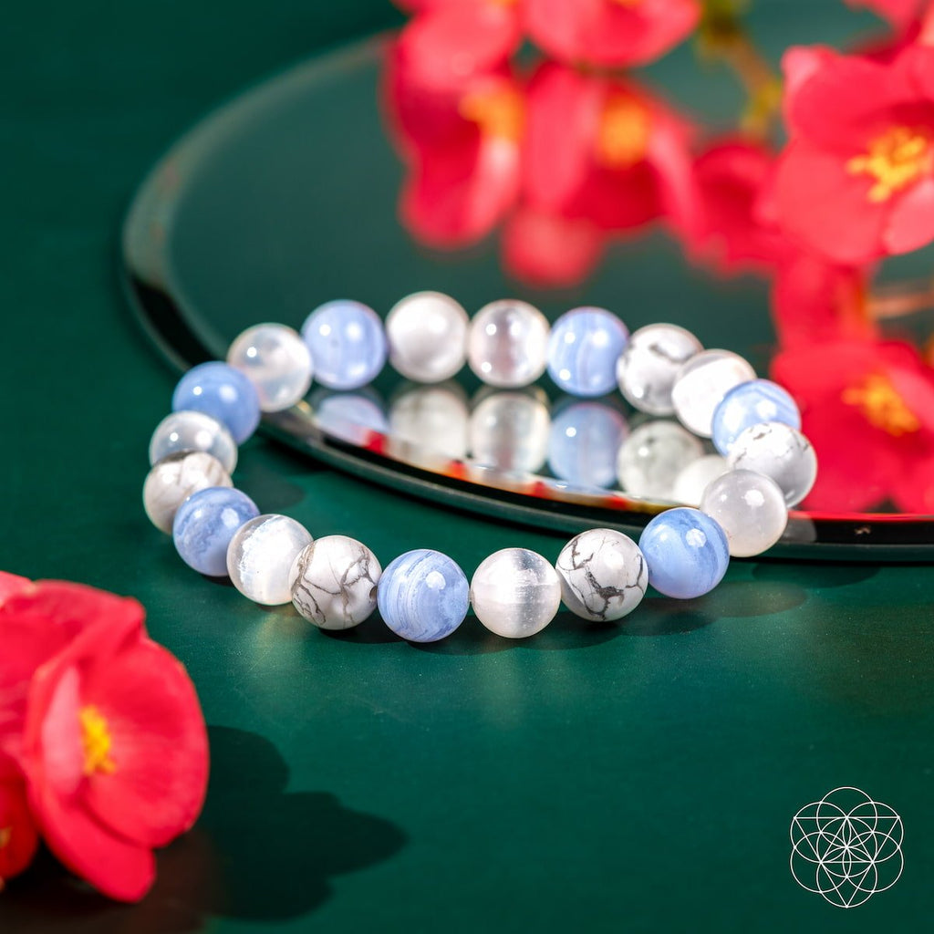 Multicolored beaded bracelet on a reflective surface with red flowers in the background