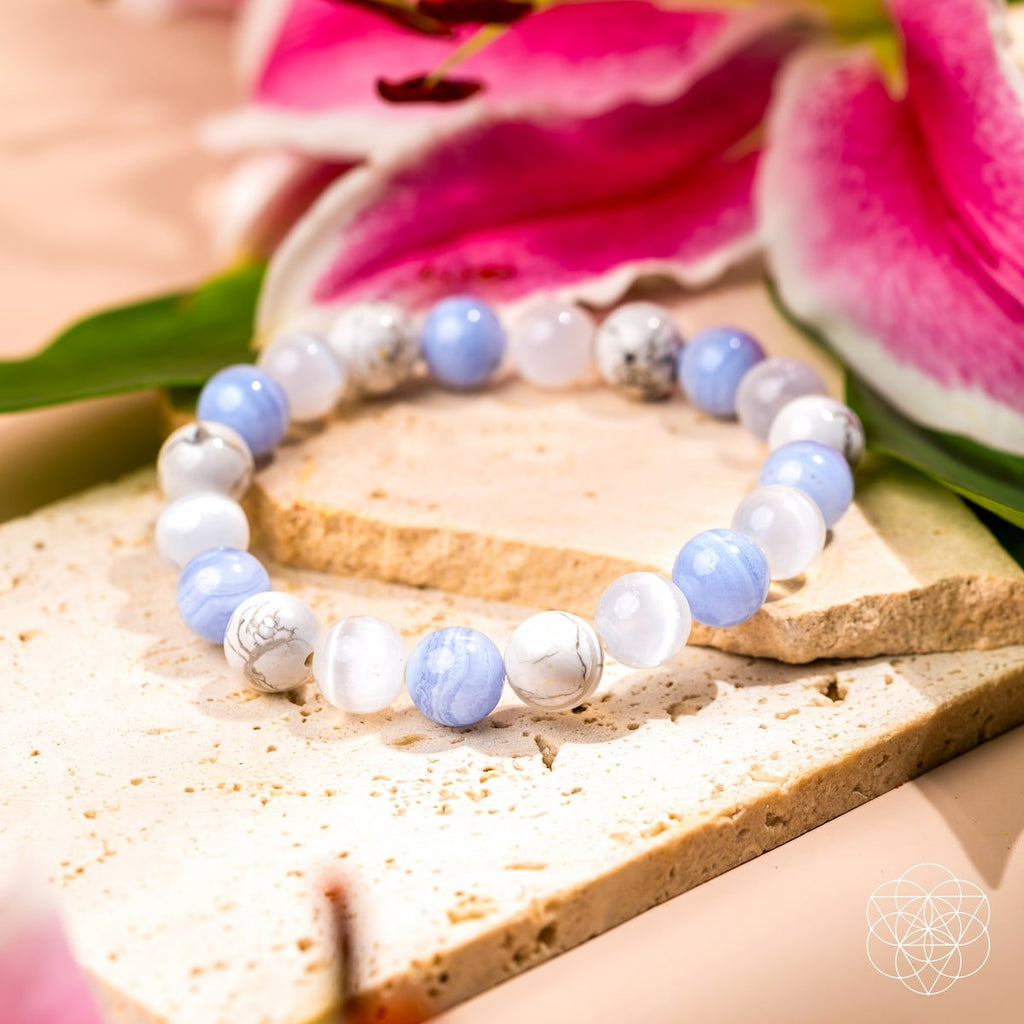 Beaded bracelet with blue and white beads on a wooden surface with pink flowers in the background